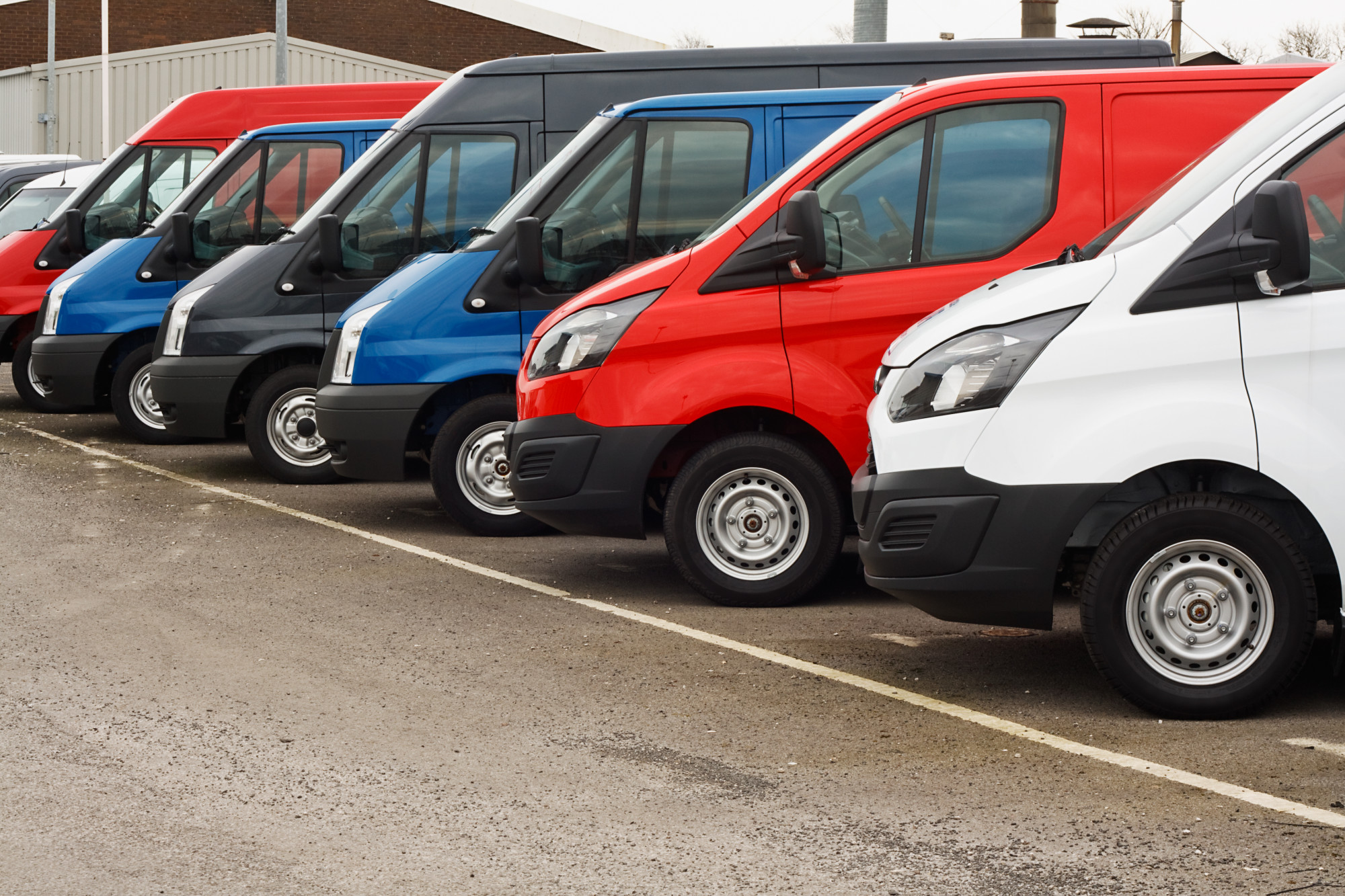 row of different marques of commercial vehicles or vans for retail sale on a motor dealers lot all logos removed