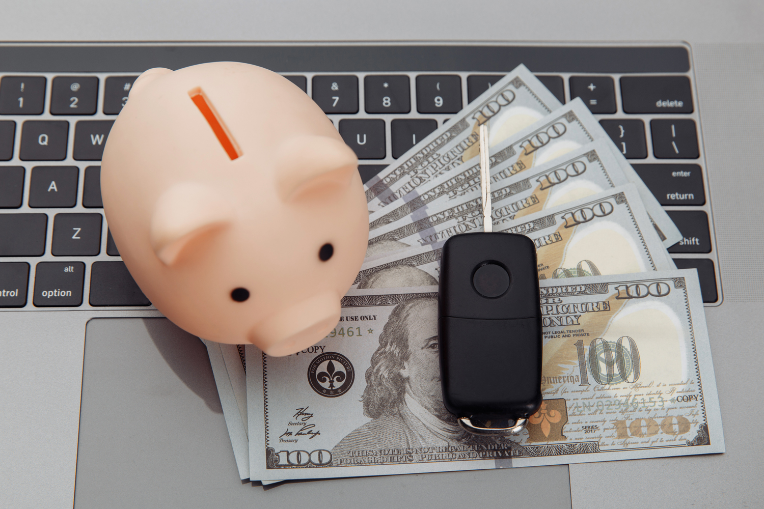 Piggybank on top of laptop with money and car remote